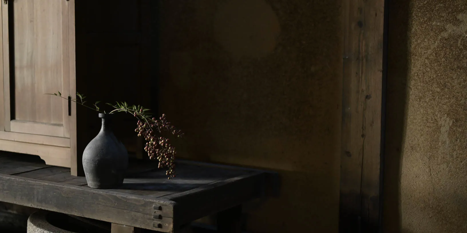 A corridor beside an earthen wall; a vase and a low table in the half-light.