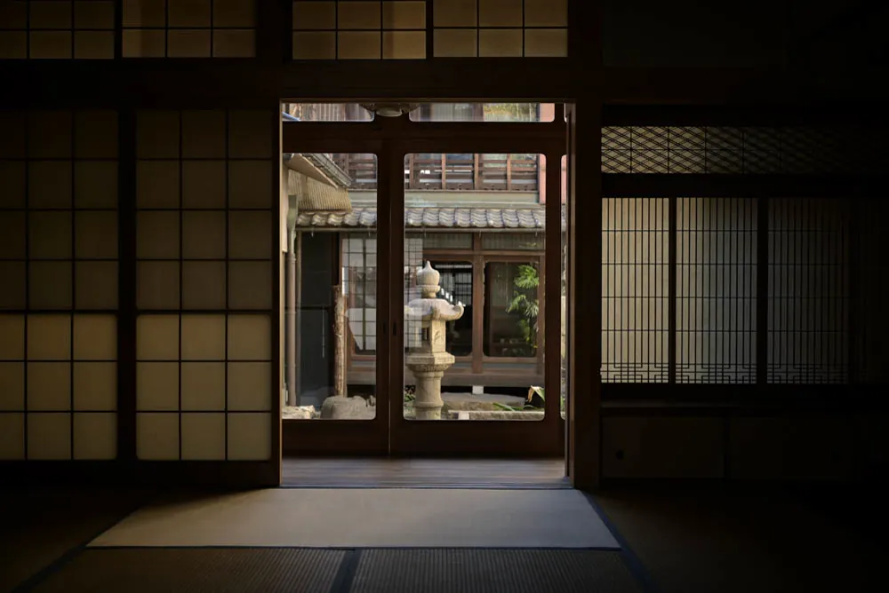 From a dark tatami room, through the glass doors, a stone lantern stands in the garden light.